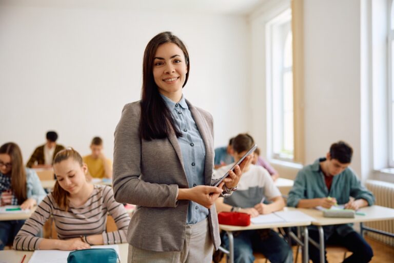 Happy female teacher in the classroom looking at camera