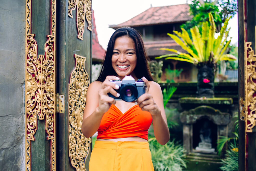 Happy young Asian female photographing on camera in exotic place