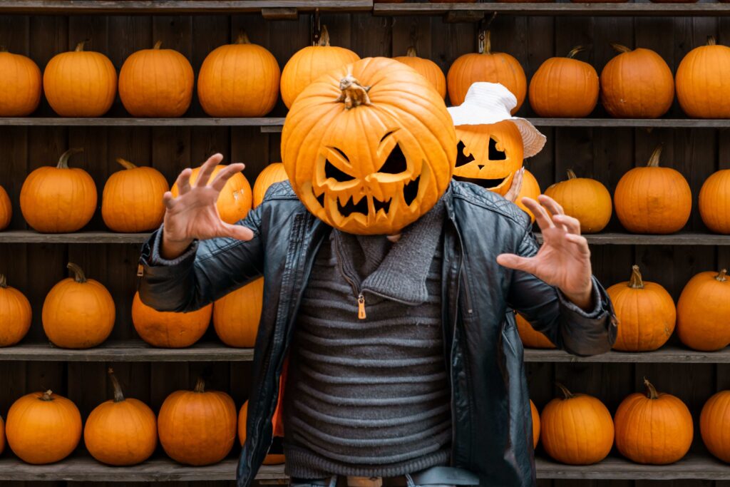 Male wearing pumpkin on head in background of pumpkins