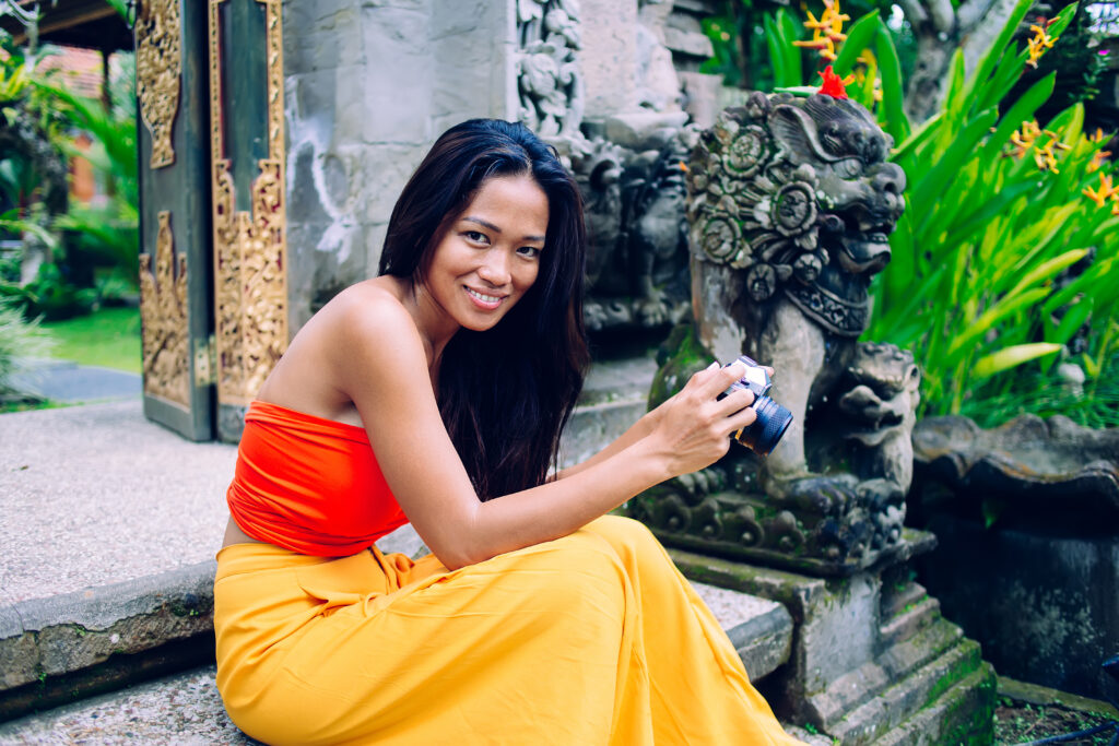 Young Asian cheerful woman sitting in oriental park with camera