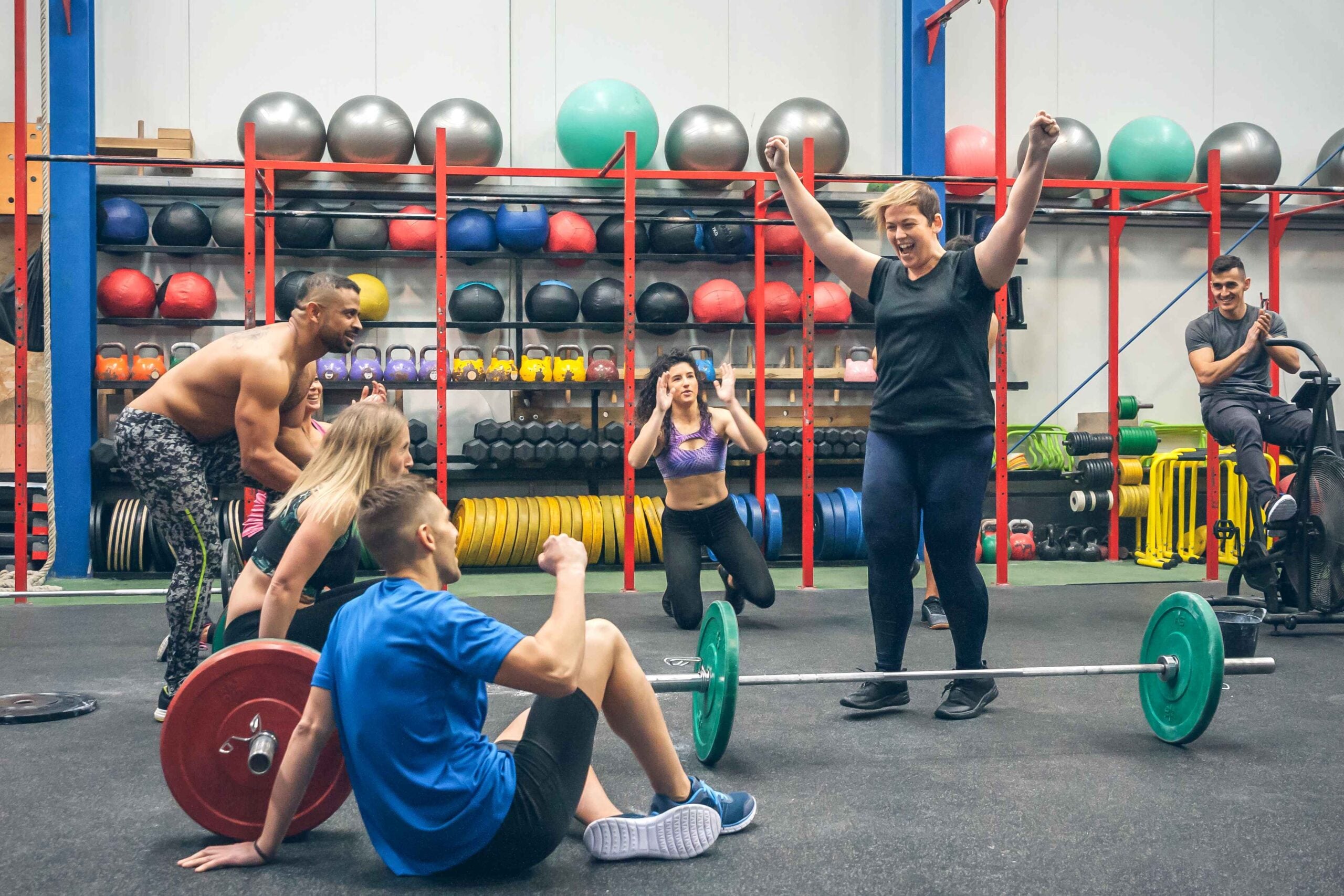 Happy woman celebrating her weightlifting achievement while her gym mates cheering her on