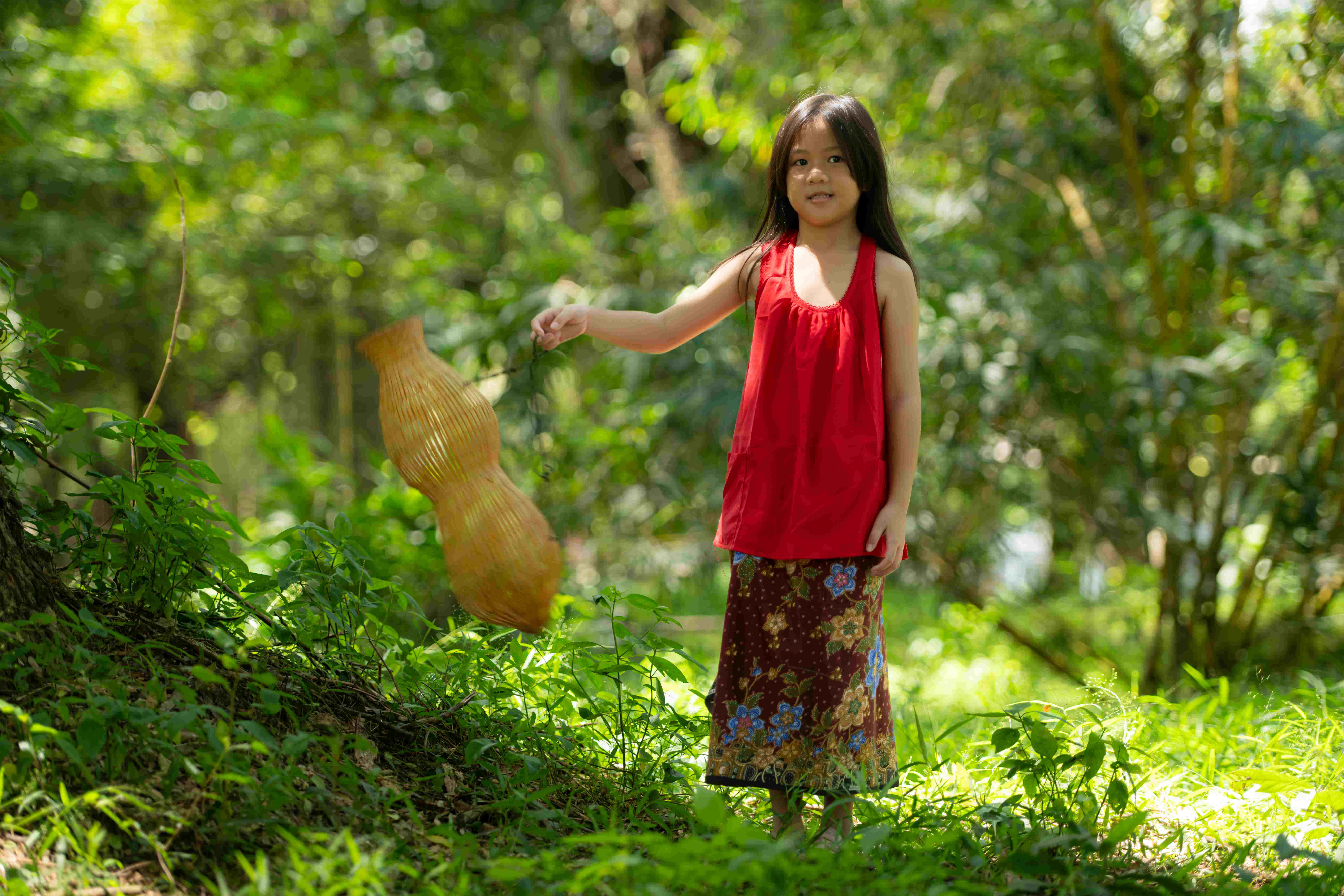 Little asian girl in red dress holding fishing equipment in the