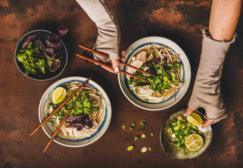 Womans hands with chopsticks and lime over vietnamese Pho Ga soup