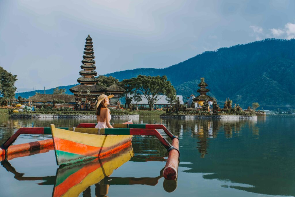 Young woman traveler paddling on a wooden boat at Pura Ulun Danu