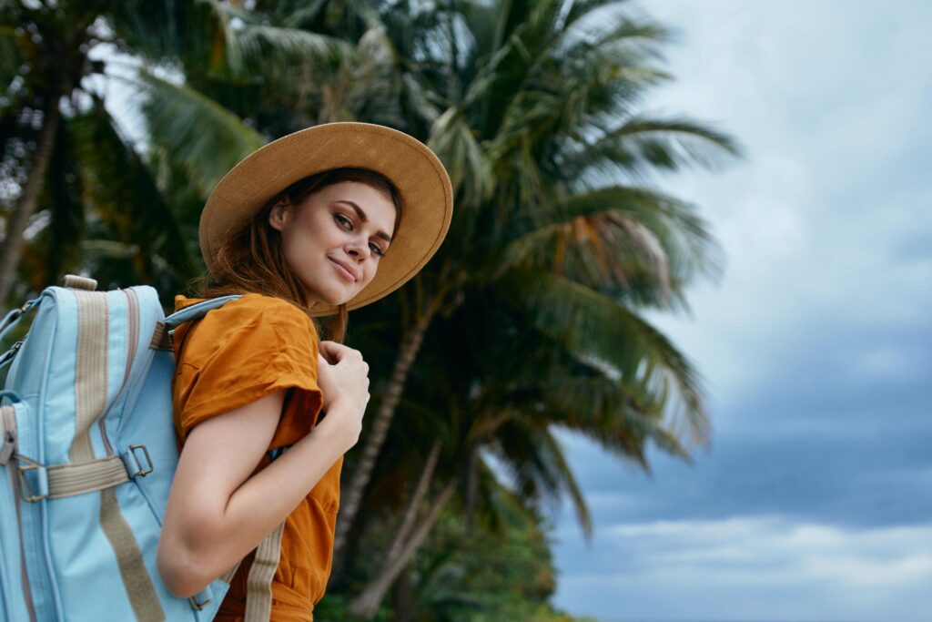 woman in a hat and with a backpack smiles at the camera on the nature on the island