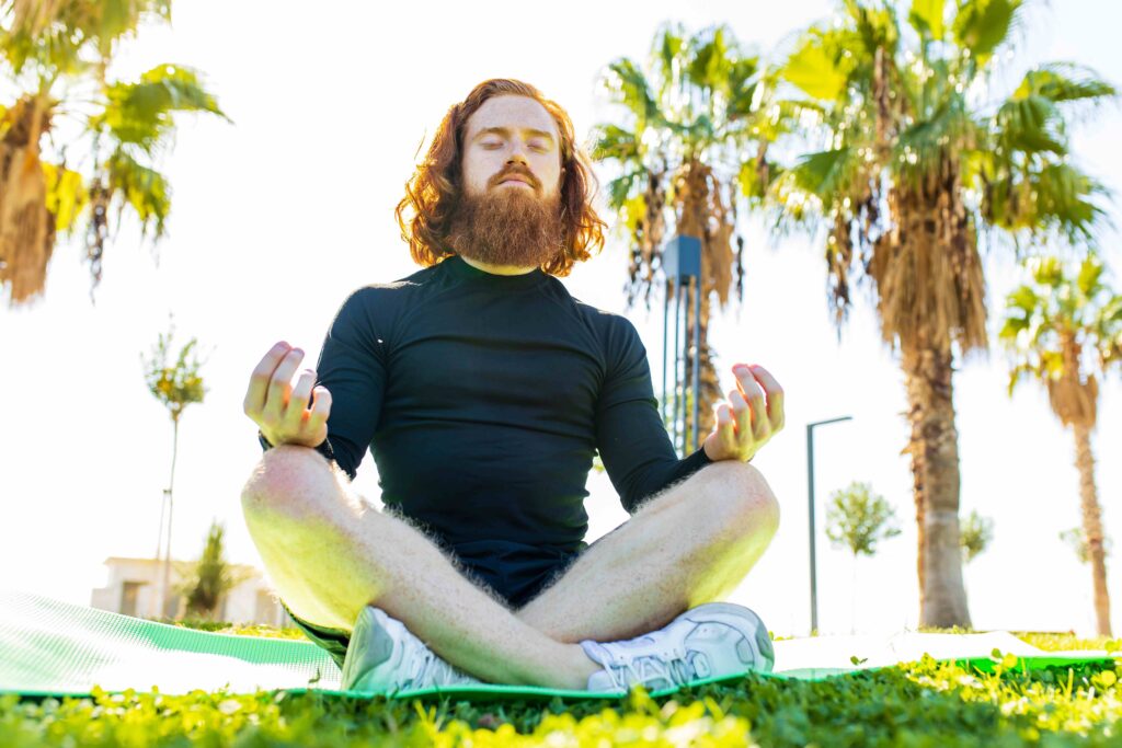 handsome redhaireb man with long beard wear black sporty suit doing yoga meditation in sunny beach