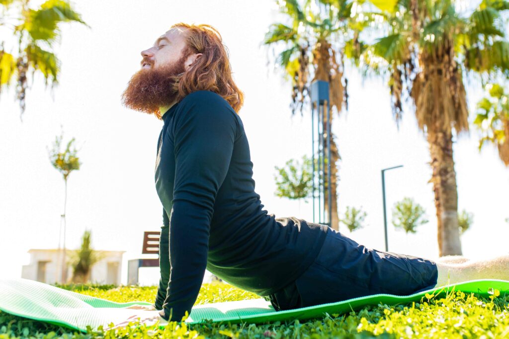 handsome redhaireb man with long beard wear black sporty suit doing yoga meditation in sunny beach