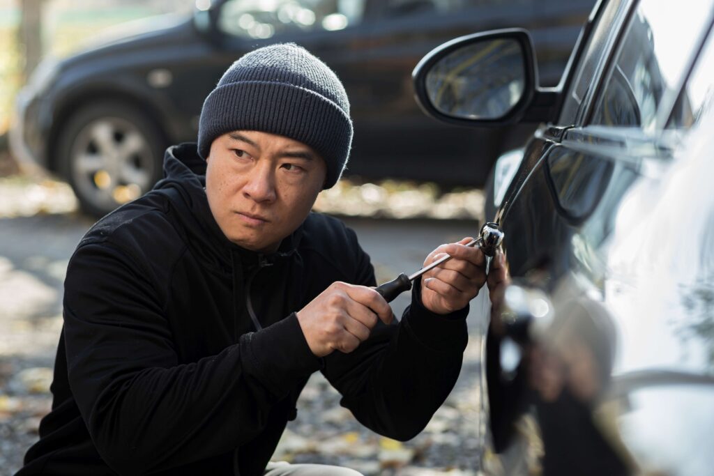 Male asian thief steals car breaks door lock with mechanical screwdriver tool
