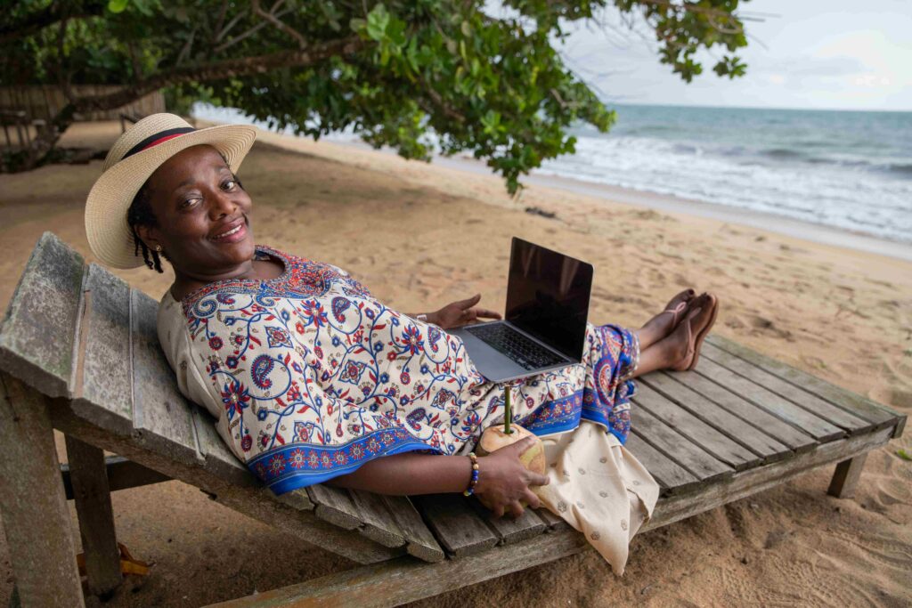 Mature woman uses her laptop lying in a hammock at a tropical beach in Africa