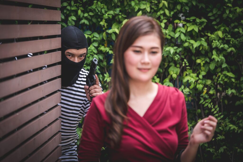Thief is holding a gun and looking at asian woman, who is walkin