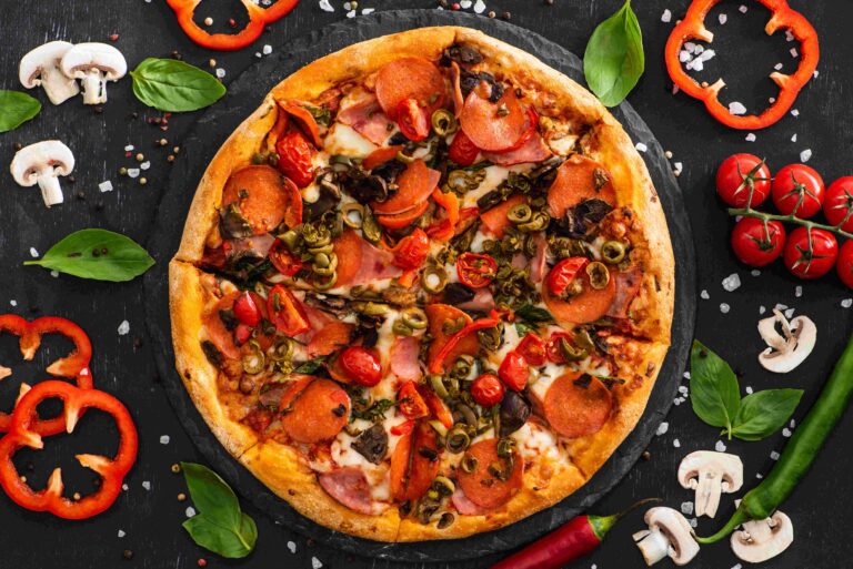 top view of delicious Italian pizza with vegetables and salami on black background