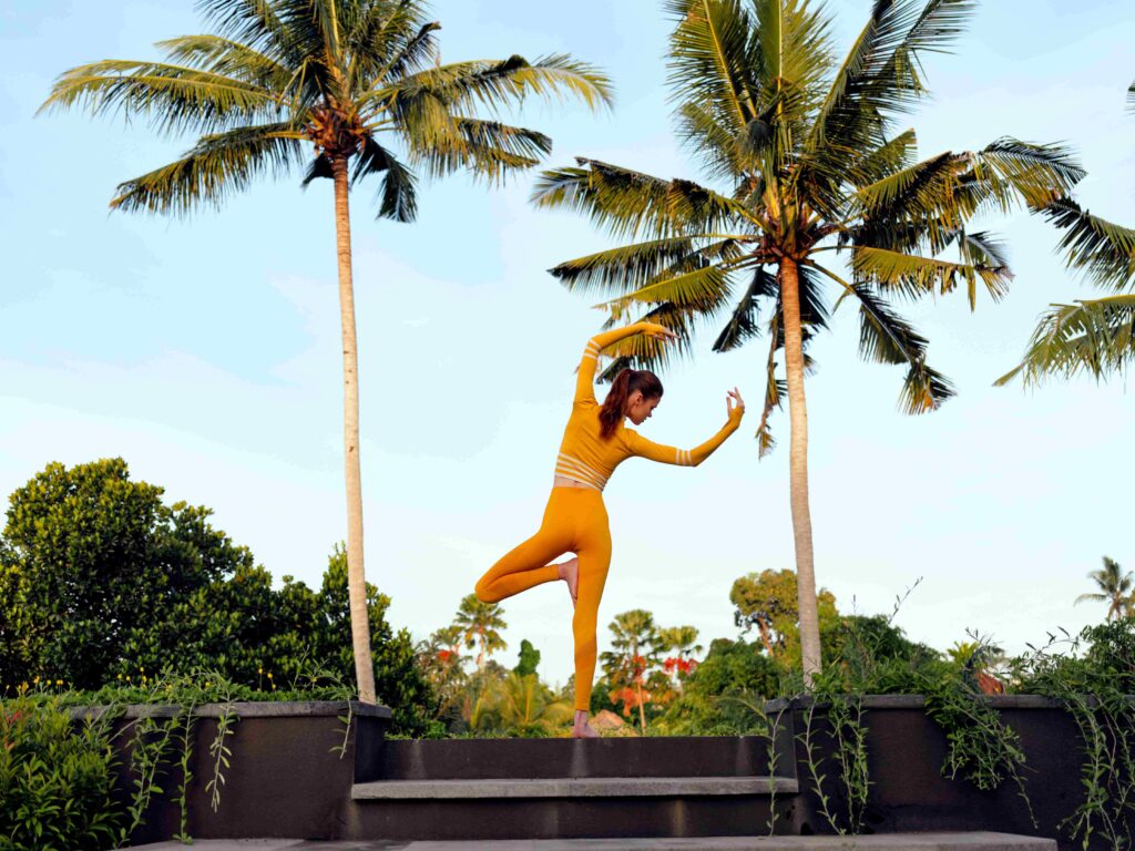 vibrant yellow suit woman nails handstand pose among lush palm trees