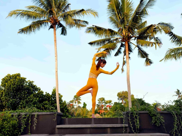 vibrant yellow suit woman nails handstand pose among lush palm trees