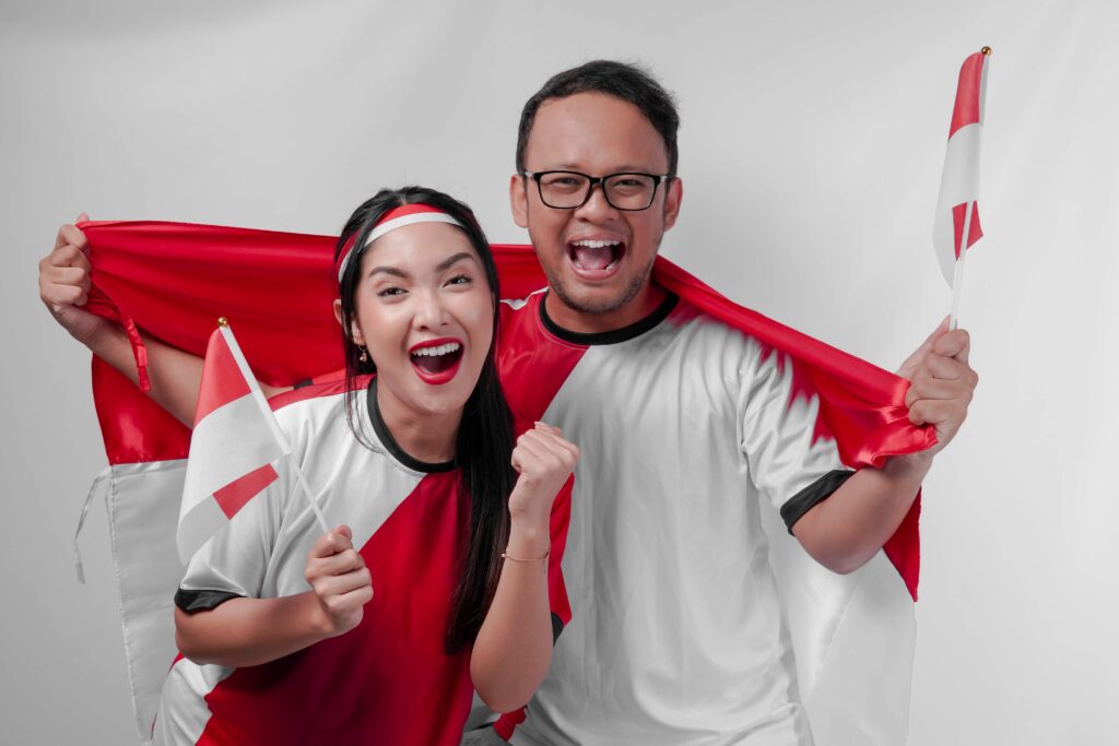 Young Indonesian couple holding country flags, feeling excited watching sport competition